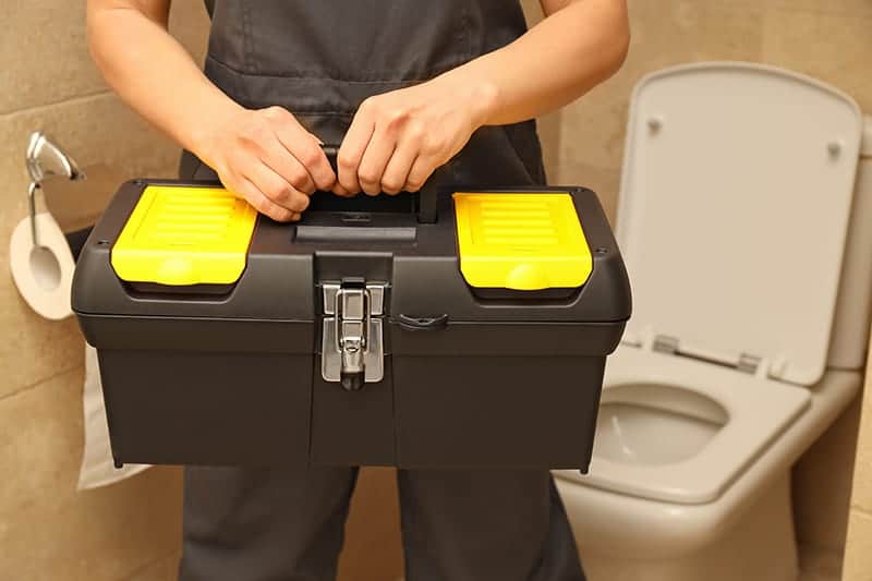 Plumber working on toiler with tool box